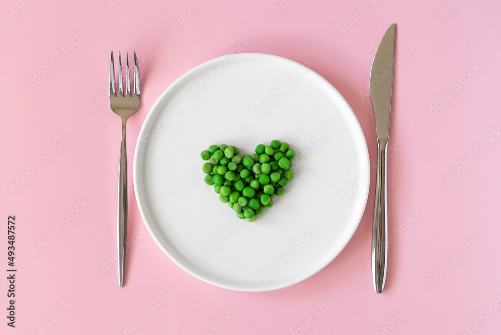 Top view of fresh green peas. Heart shaped green peas in white platel on pink background. Space to write text font Top view of fresh green peas. Heart shaped green peas in white platel on pink background. Space to write text font