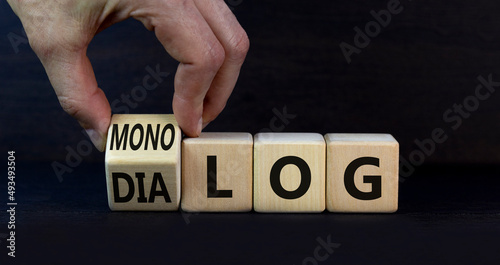 Businessman turns wooden cubes and changes the German word monolog - monologue in English to dialog - dialogue in English. Beautiful grey background. Business monolog or dialog concept. Copy space. photo