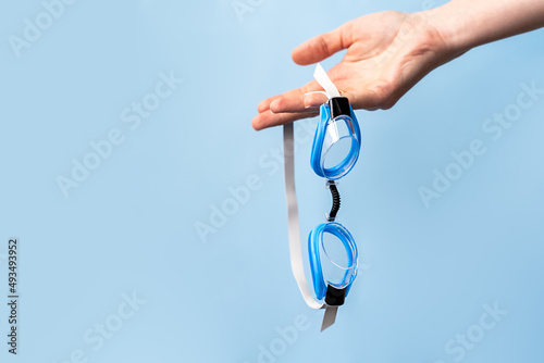 Canvas Print hand holds out goggles for swimming on a blue background, the concept of sports