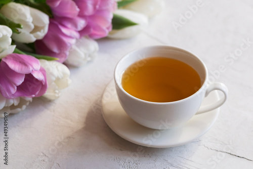 Aromatic tea in a white cup with a bouquet of fresh tulips on a light table. Close-up. Selective focus.