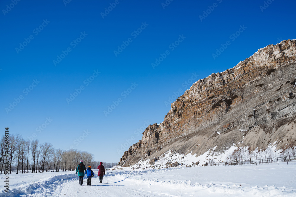A group of people of tourists walks along a snowy road in a mountainous area. Winter family trip to nature.