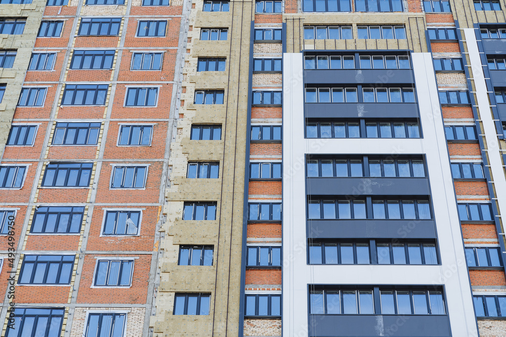 The facade of the building has windows in a brick wall. Insulation of a residential building, thermal insulation mineral wool, a rack of a residential building, facing the outside