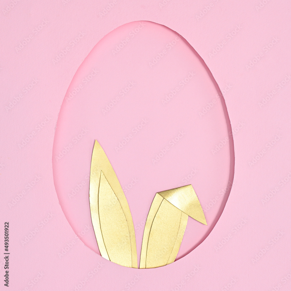 Egg shape frame with golden rabbit ears peek from hole on pastel pink background. Flat lay creative Easter concept