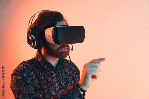 caucasian man using googgles for virtual reality and pointing in a direction in front of him. Medium Close up shot. Orange Background. High quality photo