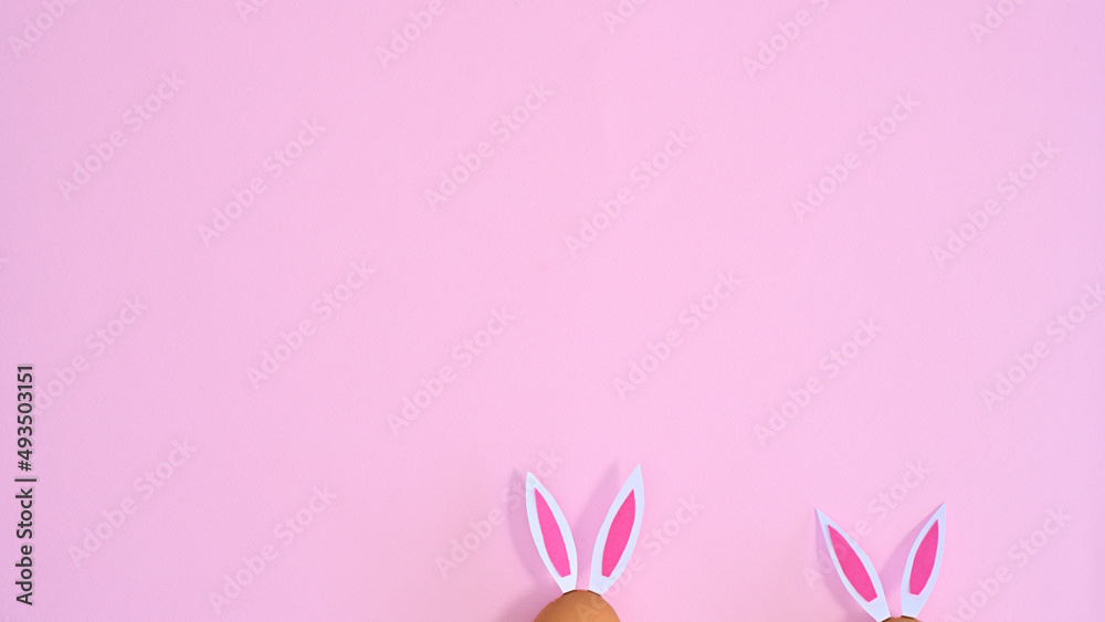 Two natural eggs with rabbit ears peek on pastel pink background with copy space. Easter flat lay minimal