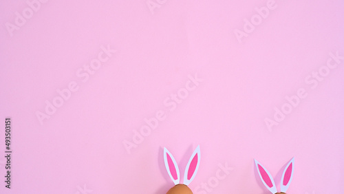 Two natural eggs with rabbit ears peek on pastel pink background with copy space. Easter flat lay minimal