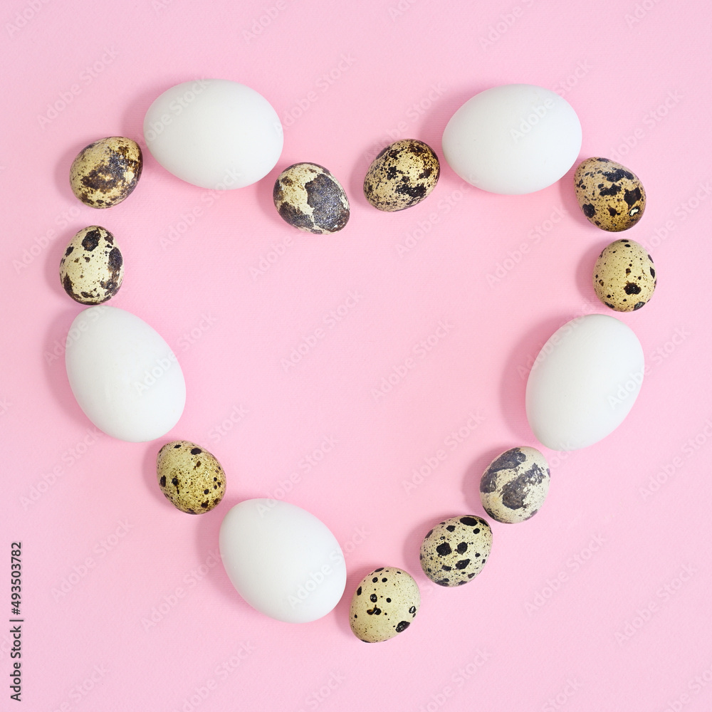 Creative copy space heart shape frame with white and quail natural eggs on pastel pink background. FLat lay