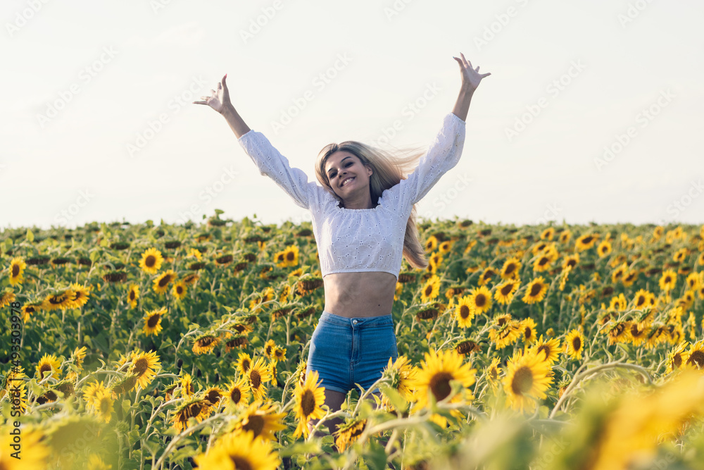 Happy long-haired blonde girl in a white blouse and denim shorts jumping in a field of sunflowers on a summer day.Summer concept,copy space. Happy long-haired blonde girl in a white blouse and denim shorts jumping in a field of sunflowers on a summer day.Summer concept,copy space.