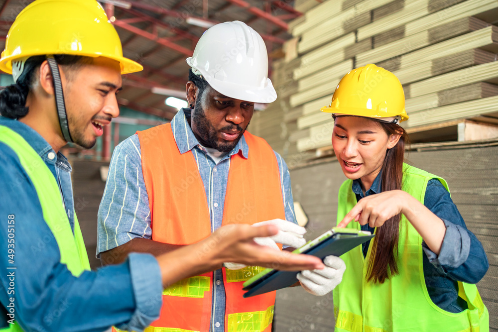 Engineer african man and asian worker wearing safety helmet and vest holding notebook and take note on the paper warehouse.Products and corrugated cardboard. Factory for the manufacture. Engineer african man and asian worker wearing safety helmet and vest holding notebook and take note on the paper warehouse.Products and corrugated cardboard. Factory for the manufacture.