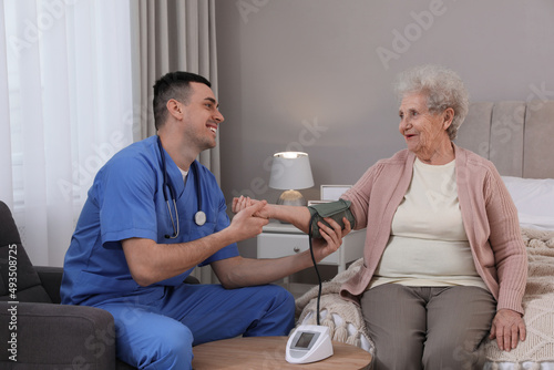 Young caregiver measuring blood pressure of senior woman in bedroom. Home health care service