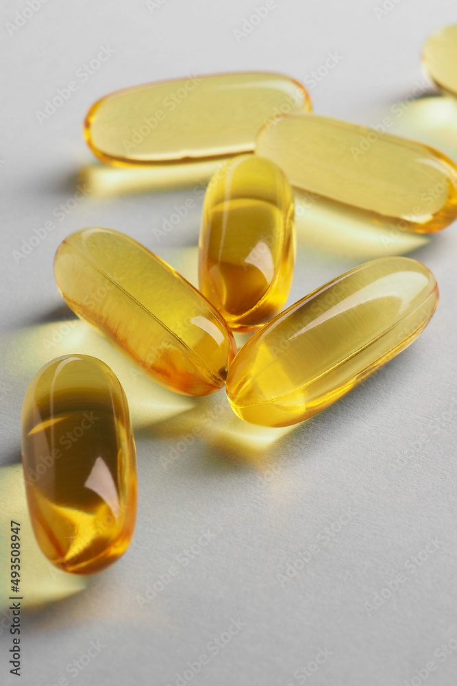 Fish oil. Yellow softgels or capsules lie on white or light gray surface. Vertical illustration about vitamins and healthy lifestyle. Softgel closeup. Omega-3 fatty acids. Macro Fish oil. Yellow softgels or capsules lie on white or light gray surface. Vertical illustration about vitamins and healthy lifestyle. Softgel closeup. Omega-3 fatty acids. Macro