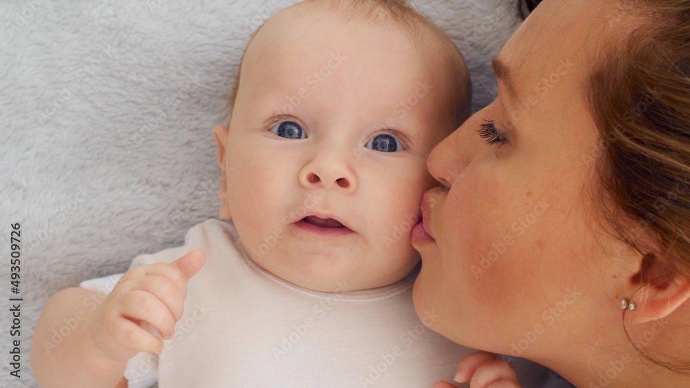 Happy newborn baby with his mother. Healthy newborn baby in a white t-shirt with mom. Closeup Faces of the mother and infant baby. Cute Infant boy and parent, top view. Happy family portrait Happy newborn baby with his mother. Healthy newborn baby in a white t-shirt with mom. Closeup Faces of the mother and infant baby. Cute Infant boy and parent, top view. Happy family portrait
