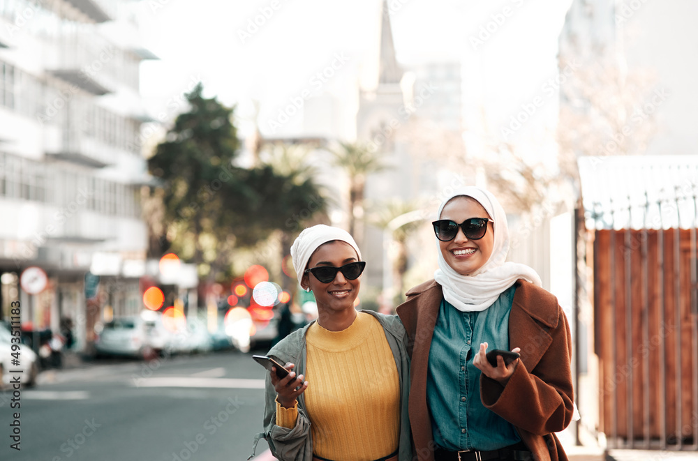 This is the millennial generation. Cropped shot of two attractive young muslim women wearing sunglasses and holding their cellphones while city sight-seeing.