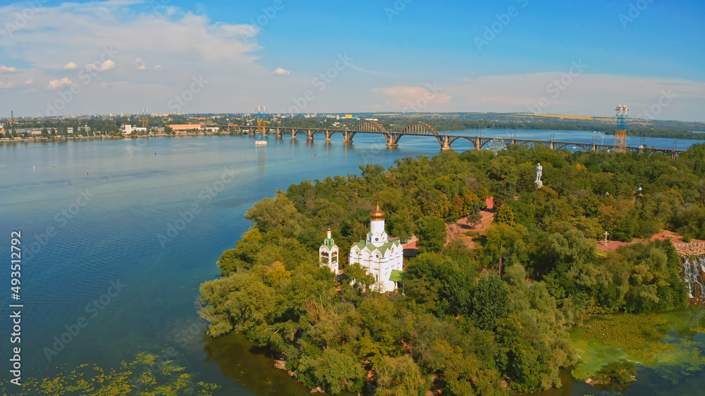 Beautiful summer landscape while sunset over the river with a church. Beautiful  urban environment - drone shooting.  Aerial view on a green island  in the town.