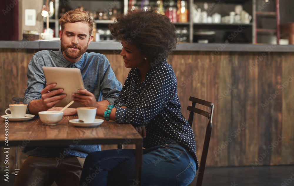 Showing him an interesting clip online. Shot of a young couple using a digital tablet together on a coffee date. Showing him an interesting clip online. Shot of a young couple using a digital tablet together on a coffee date.