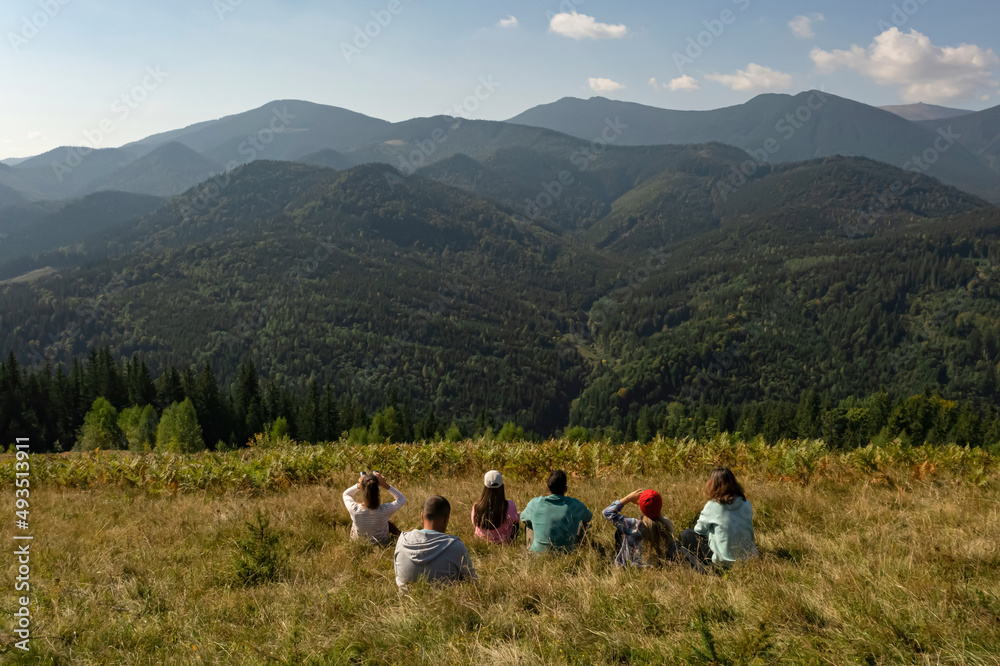 Group of tourists sitting on hill in mountains, back view