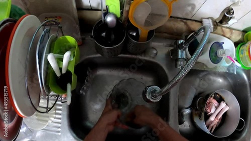 POV first person view washing a glass container in the kitchen sink with hands, water and a sponge at night in 4k