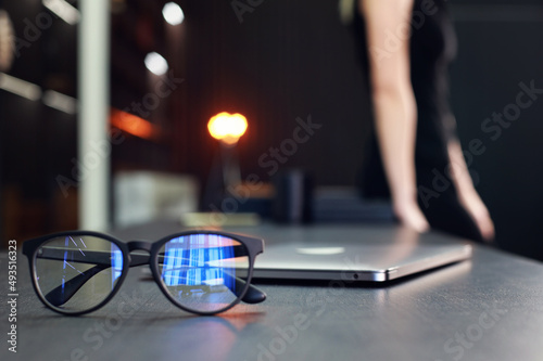 Glasses and laptop on table with woman silhouette in black.