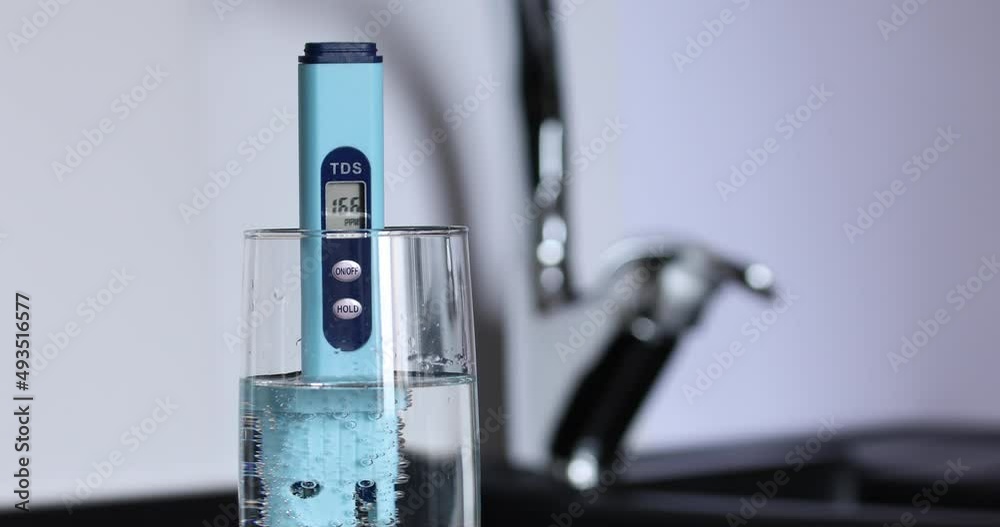 The Tds meter is in a glass with air bubbles. The concept of checking and purifying water. In the background there is a kitchen faucet and a white background The Tds meter is in a glass with air bubbles. The concept of checking and purifying water. In the background there is a kitchen faucet and a white background