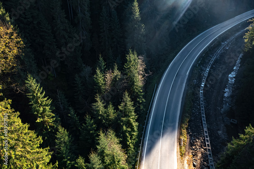 Aerial view of asphalt road surrounded by coniferous forest on sunny day. Drone photography