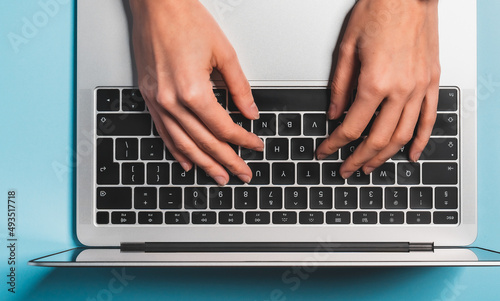 Overhead view of the working woman hands typing on keyboard notebook laptop computer at the colorful background office desk