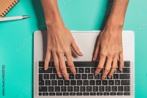 Overhead view of the working woman hands typing on keyboard notebook laptop computer at the colorful background office desk
