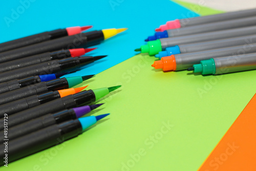 Multi-colored stationery felt-tip pens and brushes on a background of multi-colored cardboard paper.