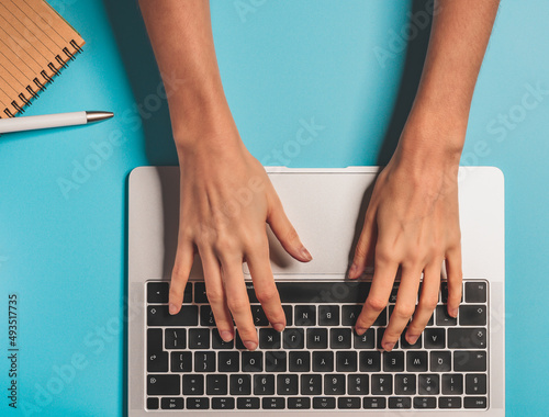 Overhead view of the working woman hands typing on keyboard notebook laptop computer at the colorful background office desk