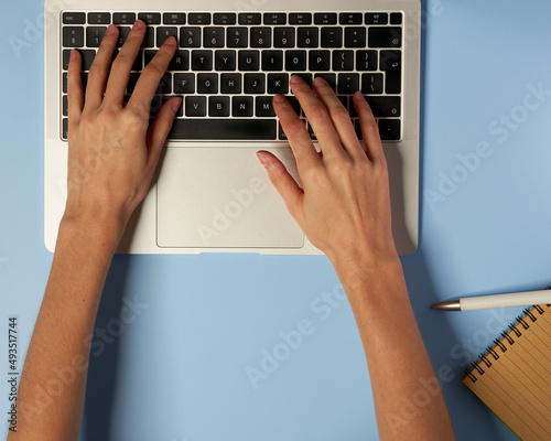 Overhead view of the working woman hands typing on keyboard notebook laptop computer at the colorful background office desk