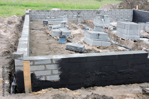 Damp proofing the outside foundation wall with a black black asphalt-based mixture, a construction site with solid concrete blocks on pallets, plastic buckets and mixing tubs photo