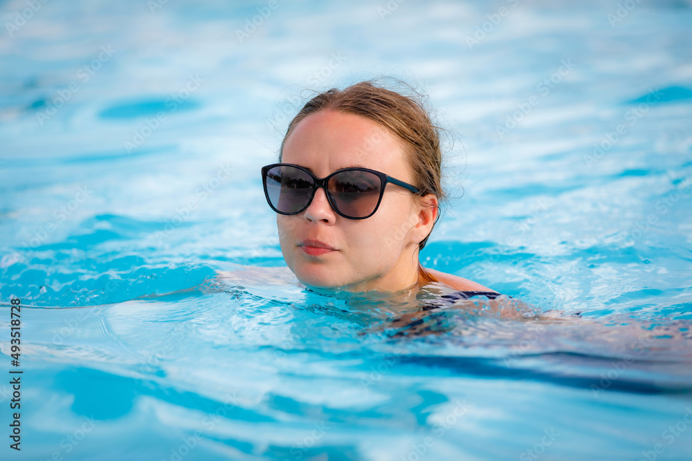 A young, beautiful girl in sunglasses swims in the pool. High quality photo