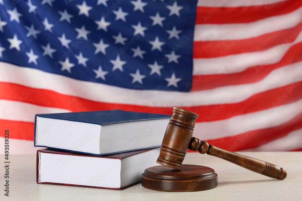 Judge's gavel and books on white wooden table against American flag