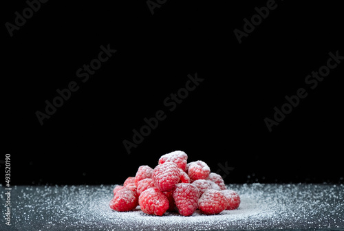 Ripe fresh raspberries with sugar powder on a gray stone table. Dark background. Close-up view. Copy space
