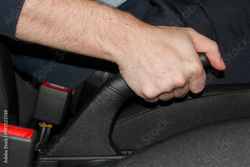 Close-up of a man's hand in a rubber glove pulling the handbrake lever in a car. The driver pulls on the handbrake in the car to activate the parking brake, the importance of the parking brake.