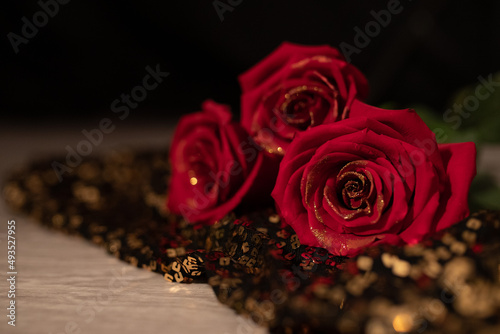 A beautiful photo of a bouquet of red roses with a golden coating on the petals, lying on a fabric with golden rhinestones. black background and gold lighting