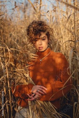 Portrait of beautiful young woman outdoor posing and holds a bouquet of reeds and looks straight at the camera