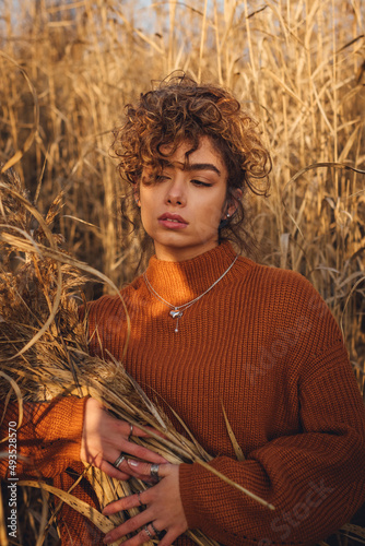 Portrait of beautiful young woman with curly hair while posing outdoor at sunset