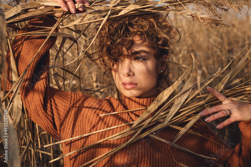 Portrait of a beautiful young woman with curly hair posing outdoor and holds bouquet of reeds over her head