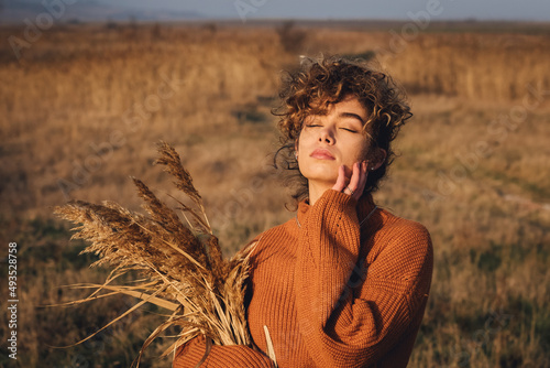 Portrait of a beautiful young female while enjoying the sun with closed eyes in the field of grass at sunset
