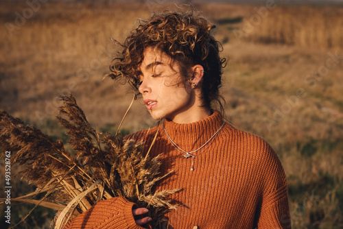 Portrait of a beautiful young woman while enjoying the sun with closed eyes in the field of grass at sunset