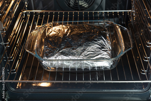 Glass tray with piece of meat wrapped in aluminum foil baked  in the oven.