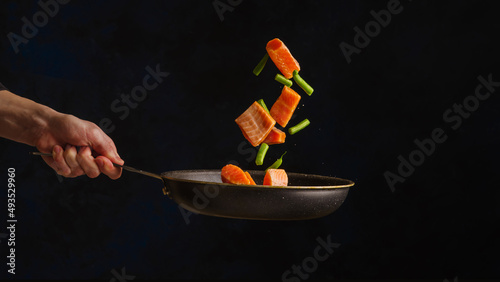 Sea food. Pieces of red fish - trout, salmon with vegetables in a pan in a frozen flight. Isolated on black background. Restaurant, hotel, cookbook, recipes. Advertising, banner.