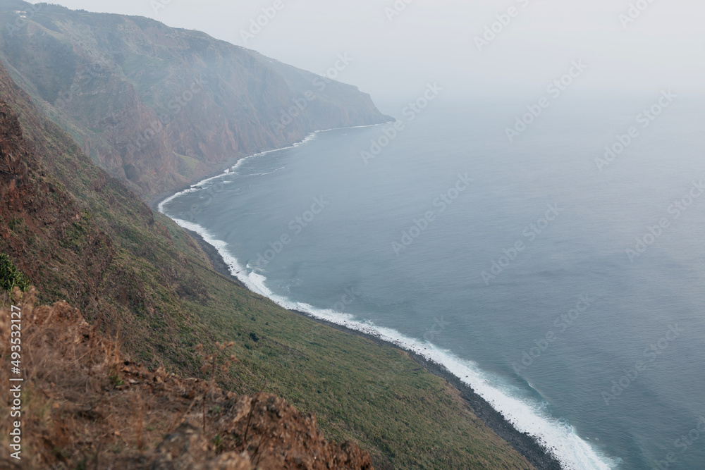 Wide coastline of ocean connected with green hills in morning fog. Wild nature of edge of Europe