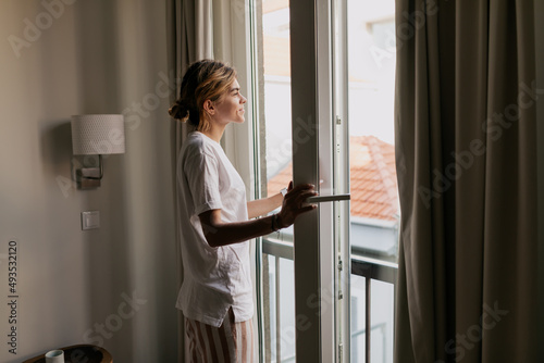 Obraz na płótnie Morning at home. Young woman in pajamas is opening balcony and looking in the window in the morning in sunny warm summer day. Wake up in the morning at home w salonie