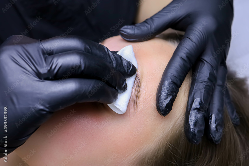 Fototapeta premium close-up of the master's hand in black gloves removes the compositions for laminating eyebrows with a napkin
