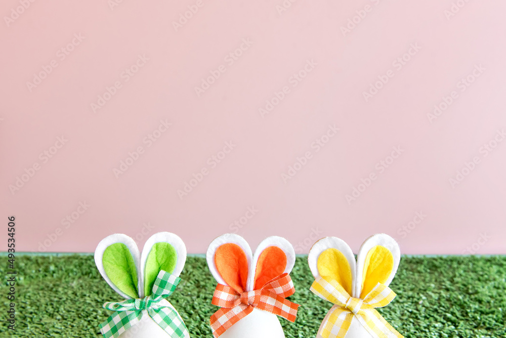 Easter decoration on pink background, colorful easter eggs with bunny ears.