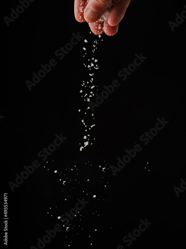 Small salt crystals in frozen flight on a black background. Minimalism. Abstraction. Cooking, recipes, ingredient for different dishes. Restaurant, hotel, cafe. Advertising, banner.