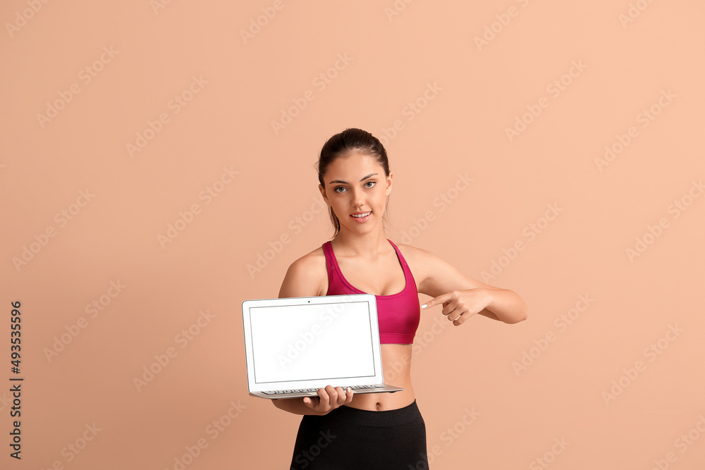 Sporty teenage girl pointing at laptop on beige background