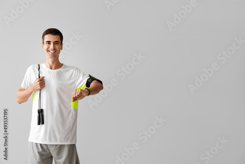 Sporty young man with jumping rope and fitness tracker on grey background