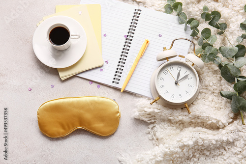 Sleep mask, notebook, cup of coffee and alarm clock on light background